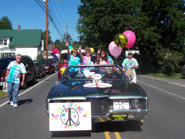 alumni dressed as hippies giving the peace sign from a classic car